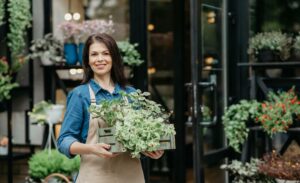 brunette woman holding a crate of plants and smiling because she knows how to make money gardening