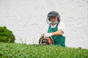 older man wearing protective gear while performing yard work for his lawn care business