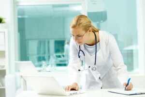 female doctor in white coat looking up information on computer to avoid HIPAA violations