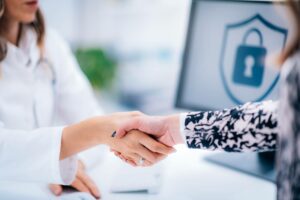 patient and doctor shaking hands while information covered under the HIPAA privacy rule remains secure on computer in the background